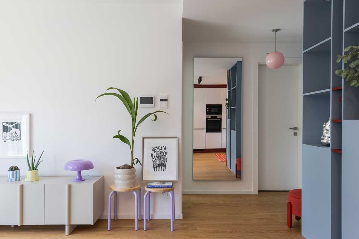 Nízká komoda a malé stolky s rostlinou a lampou vytvářejí u vstupu do bytu lehkou a hravou kompozici.