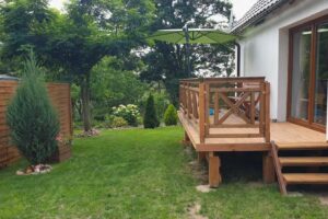 Dřevěná terasa u rodinného domu s výhledem do zelené zahrady u lesa