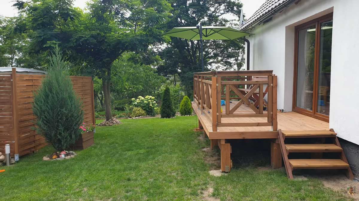 Dřevěná terasa u rodinného domu s výhledem do zelené zahrady u lesa