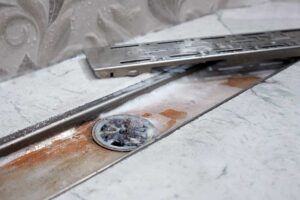 Ucpaný sprchový odtok s usazeninami a vlasy zpomalující odtok vody.