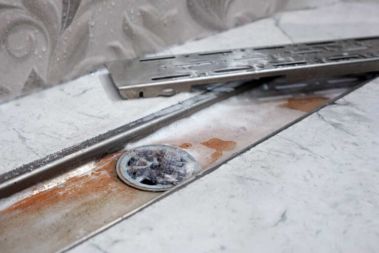 Ucpaný sprchový odtok s usazeninami a vlasy zpomalující odtok vody.