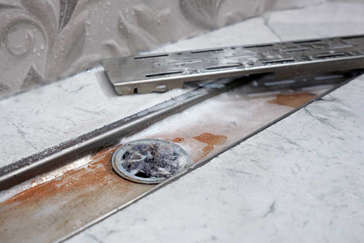 Ucpaný sprchový odtok s usazeninami a vlasy zpomalující odtok vody.