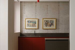 Kuchyňský kout s červenou linkou, betonovou stěnou a minimalistickým řešením