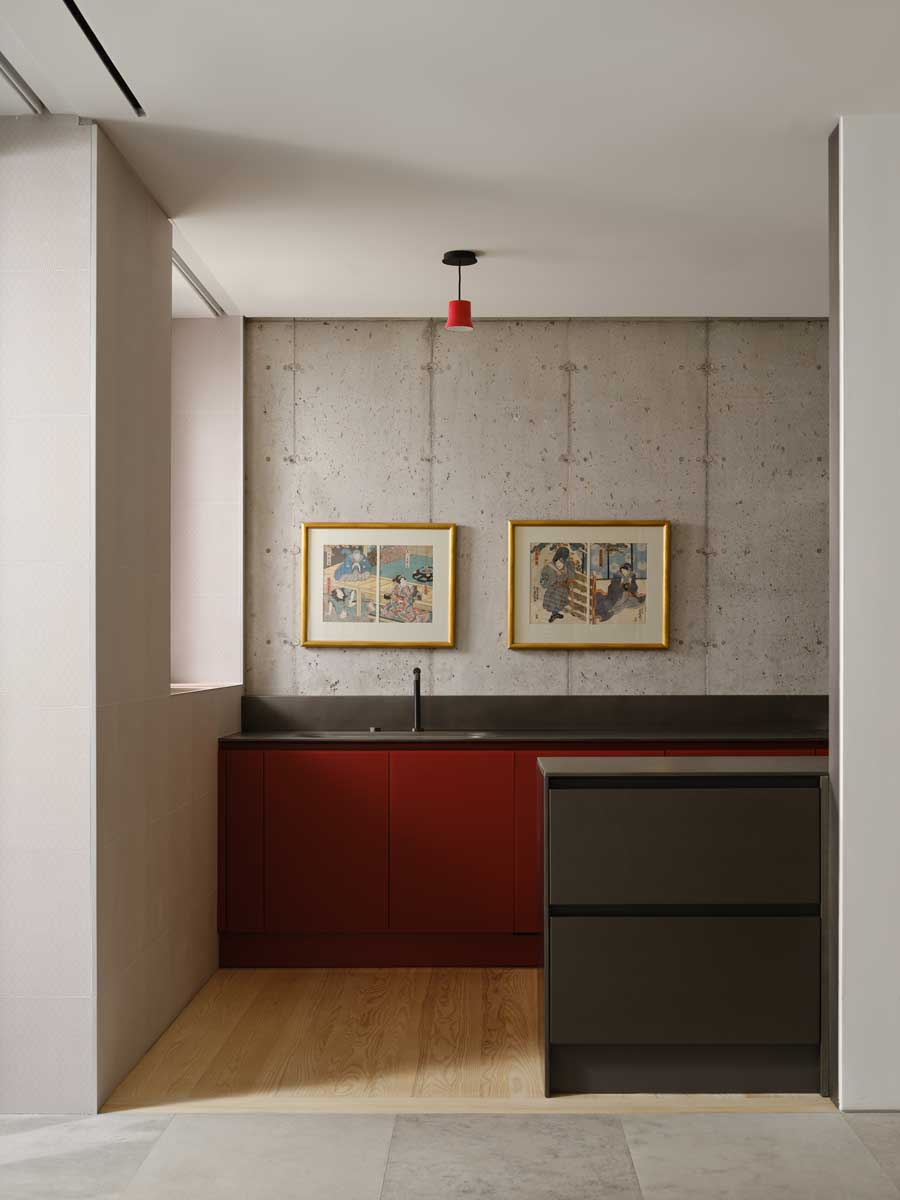 Kuchyňský kout s červenou linkou, betonovou stěnou a minimalistickým řešením