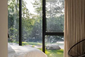 Ložnice s velkým oknem od podlahy ke stropu a výhledem do lesa a na jezero.