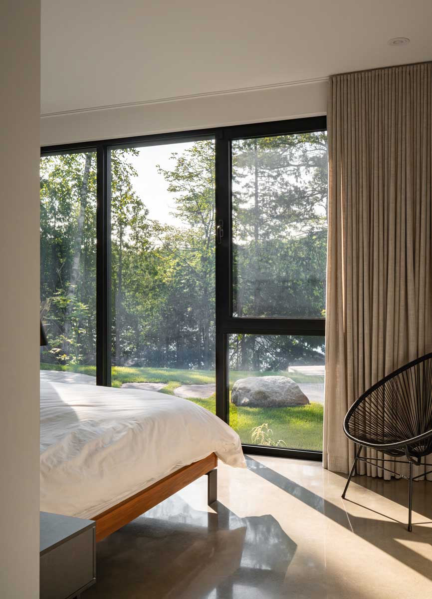 Ložnice s velkým oknem od podlahy ke stropu a výhledem do lesa a na jezero.