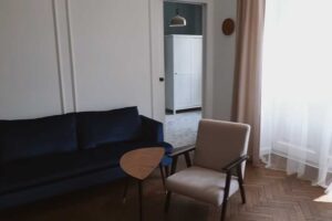 Obývací pokoj s modrou pohovkou, křeslem a renovovanými parketami v klasickém stromečkovém vzoru.