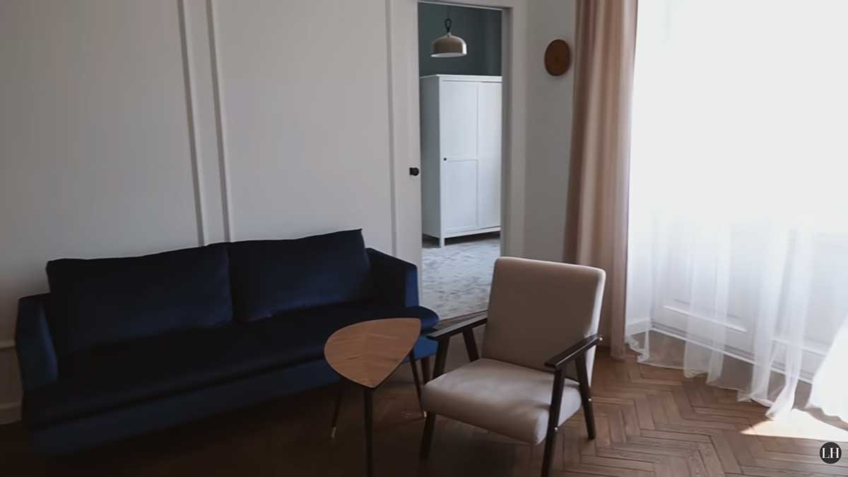 Obývací pokoj s modrou pohovkou, křeslem a renovovanými parketami v klasickém stromečkovém vzoru.