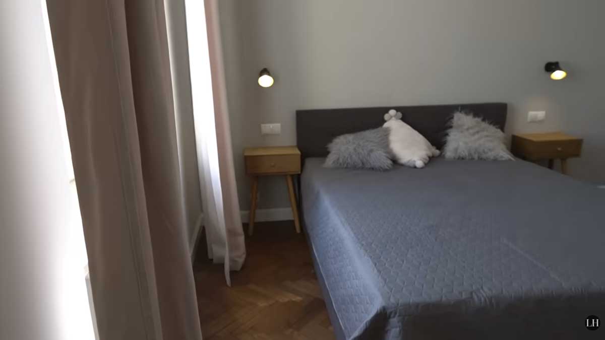 Ložnice po rekonstrukci s velkou postelí, jednoduchými nočními stolky a jemnými textiliemi u okna.