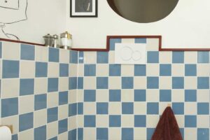 Toaleta s modrobílými čtvercovými obklady doplněná bidetem a kulatým okénkem ve stěně.