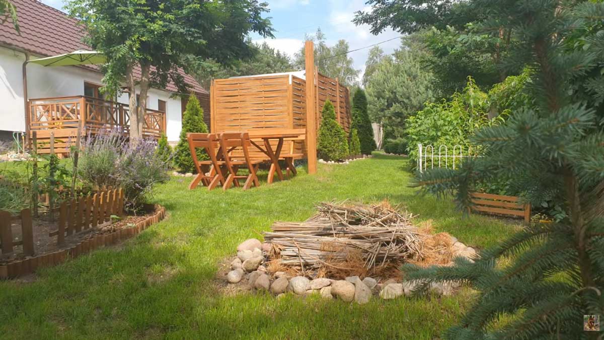 Zahrada u domu s jednoduchým ohništěm a dřevěným posezením