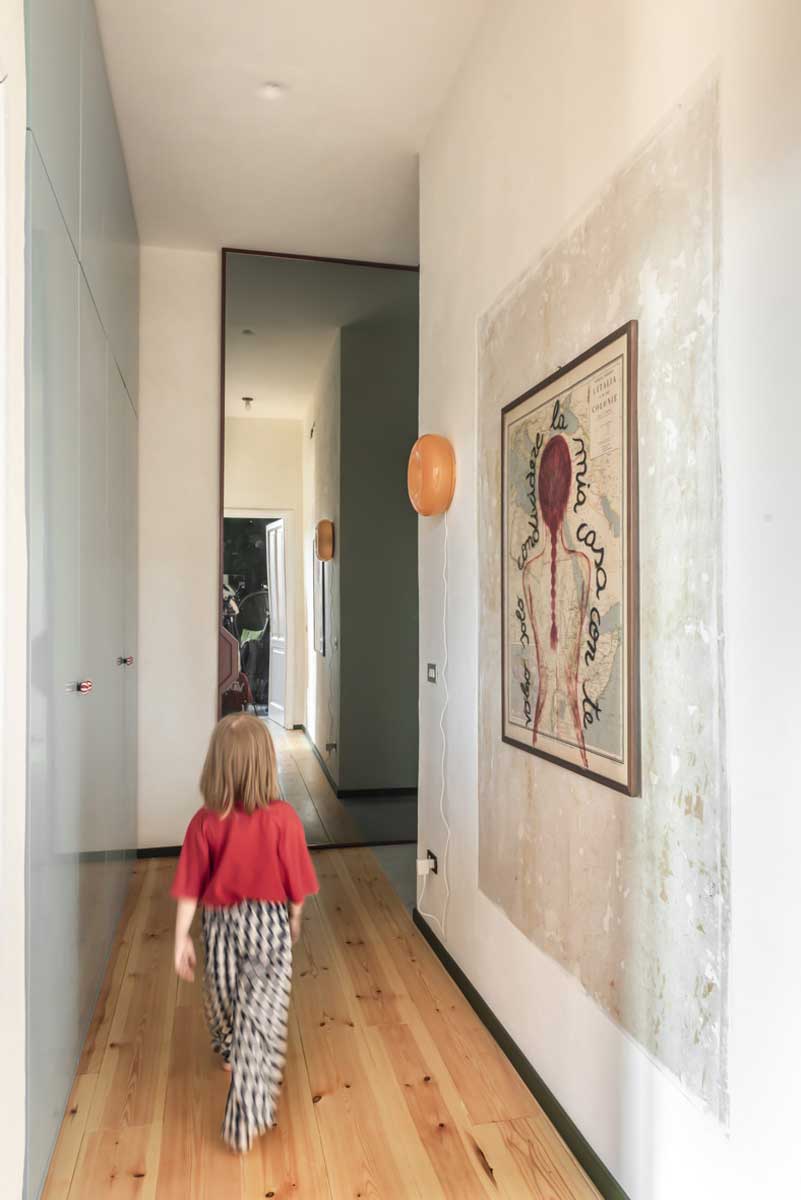 Dlouhá chodba s dřevěnou podlahou velkým zrcadlem a obrazem na světlé stěně.