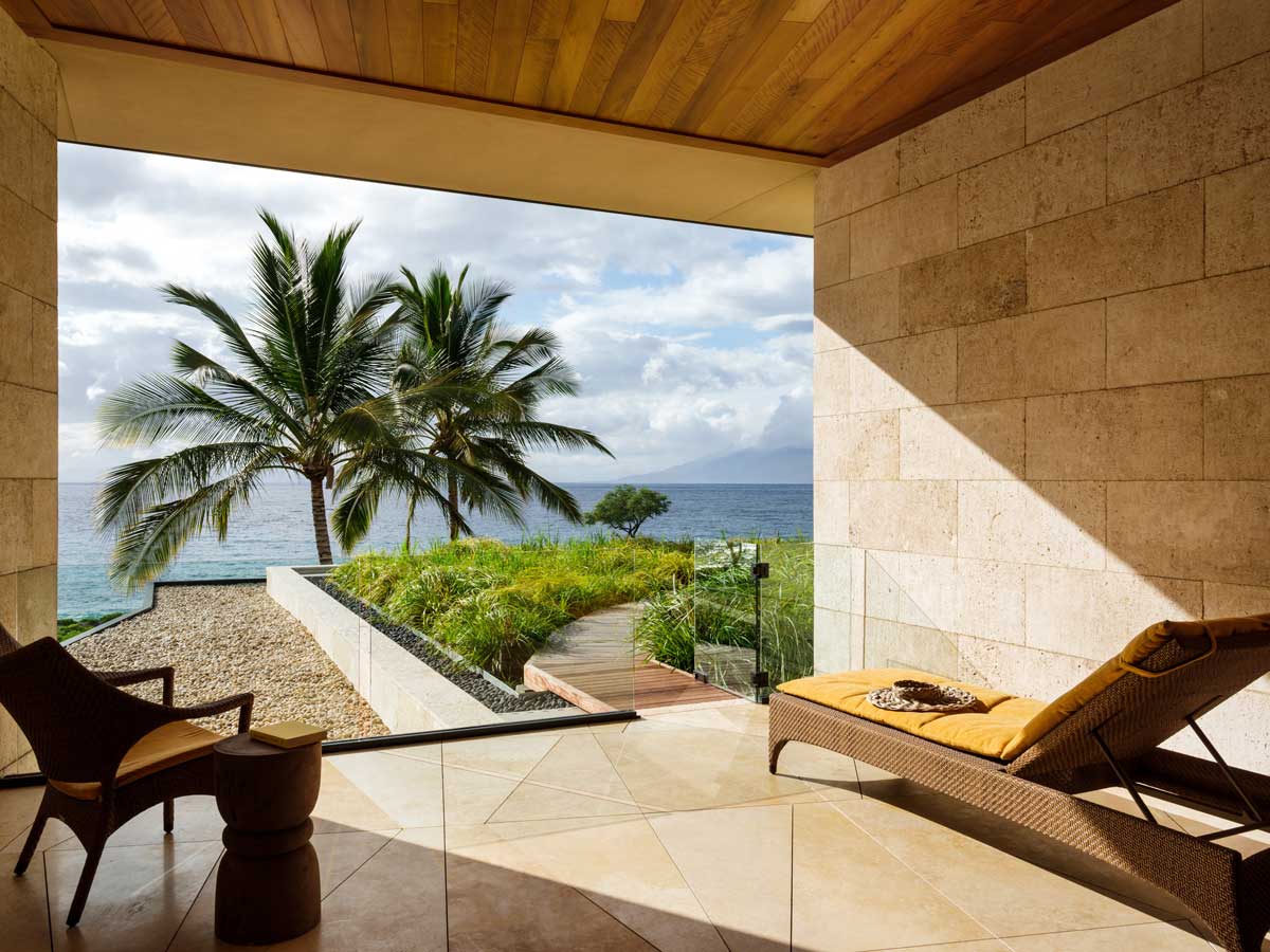 Krytá terasa s lehátkem a výhledem na oceán a palmy v tropické zahradě