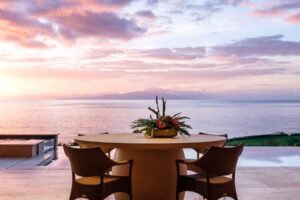 Venkovní jídelní prostor s výhledem na oceán při západu slunce.