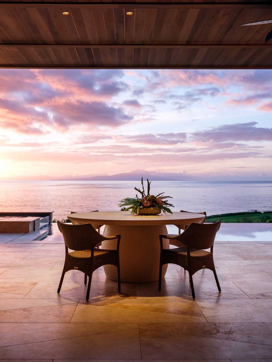 Venkovní jídelní prostor s výhledem na oceán při západu slunce.