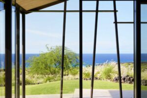 Relaxační křeslo u velkého prosklení s výhledem na oceán a zahradu