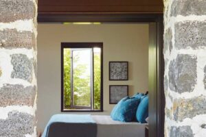 Pohled do ložnice skrze kamennou zeď s oknem a přírodními textiliemi