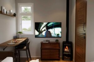 Obytný prostor tiny house s jídelním stolem, televizí a krbovými kamny.