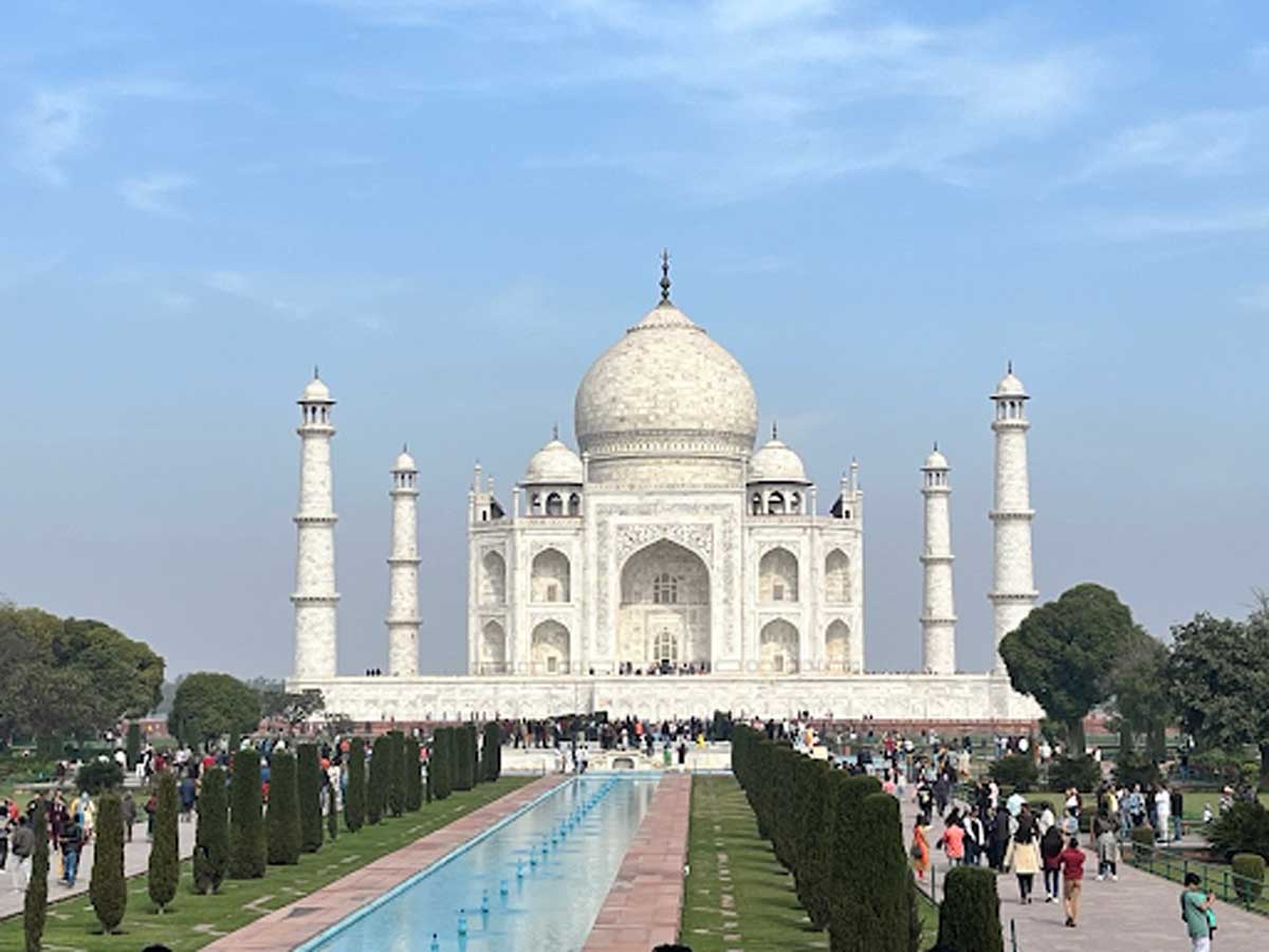 Tádž Mahal v Indii při denním světle s turisty procházejícími se kolem slavného památníku.