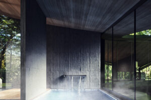 Soukromý onsen s horkou vodou navazuje na tmavé materiály wellness zóny a nabízí výhled do okolního lesa.