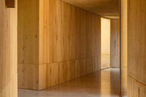 Minimalistická chodba s dřevěnými stěnami a světlem pronikajícím z exteriéru.