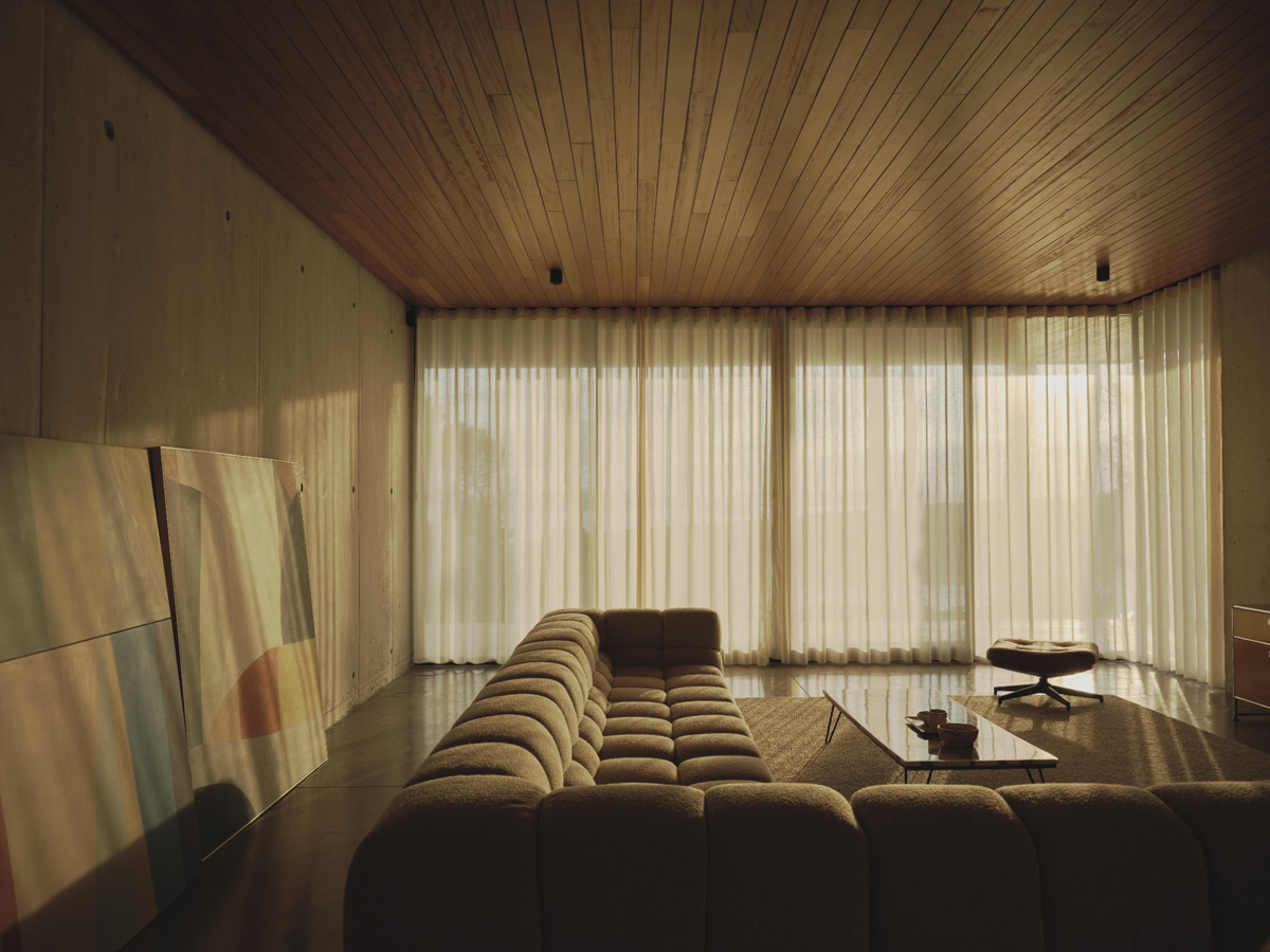 Tlumeně osvětlený obývací pokoj s měkkou pohovkou a vysokými závěsy působí klidně a útulně.