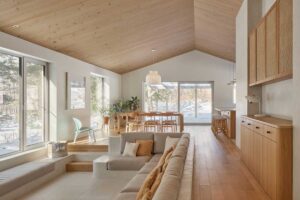 Otevřený interiér s velkými okny, jídelním stolem a kuchyní plynule navazuje na okolní lesní krajinu