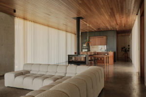 Prostorná denní zóna s designovým krbem, kuchyní a velkou pohovkou působí vzdušně a elegantně.