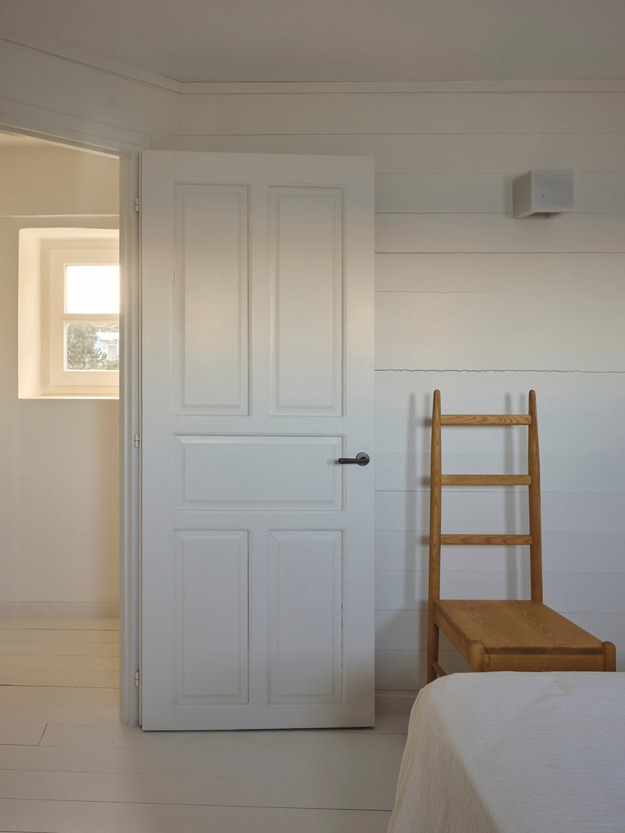 Bílé kazetové dveře vedle dřevěné židle v minimalistickém interiéru.