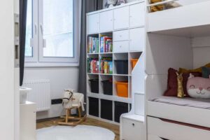 Dětský pokoj s patrovou postelí úložnými prostory a světlým nábytkem působí prakticky a zároveň hravě.