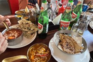 Tradiční indické jídlo servírované na stole s naanem, omáčkami a pivem Kingfisher.