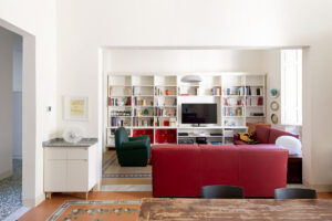 Pohled z jídelny do obývacího pokoje ukazuje otevřenou dispozici, vestavěnou knihovnu a výrazné barevné akcenty.