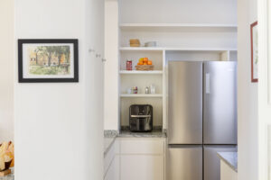 Nikový kout v kuchyni s nerezovou lednicí, policemi a kávovarem využívá prostor prakticky i elegantně.