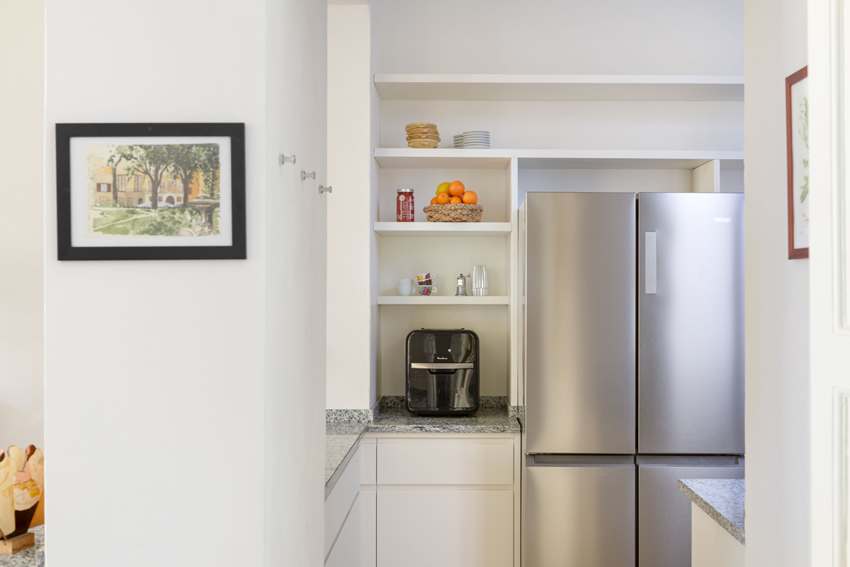 Nikový kout v kuchyni s nerezovou lednicí, policemi a kávovarem využívá prostor prakticky i elegantně.