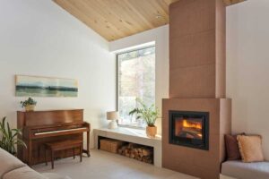 Obývací kout s klavírem, krbem a velkým oknem vytváří útulnou atmosféru propojenou s přírodou