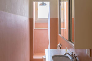 Úzká koupelna v teplých pudrových tónech kombinuje mramorovou desku, jemné světlo a italskou eleganci.