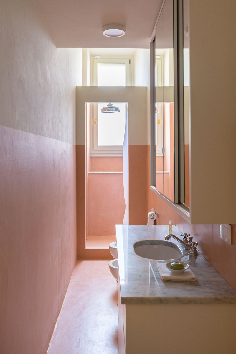 Úzká koupelna v teplých pudrových tónech kombinuje mramorovou desku, jemné světlo a italskou eleganci.