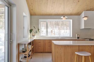 Kuchyň s dřevěnými skříňkami, velkým oknem a světlými povrchy působí čistě a nadčasově