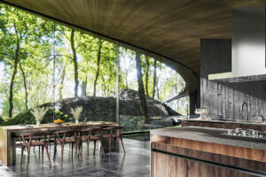 Otevřená kuchyně s jídelnou využívá panoramatické prosklení, které mění les v přirozenou kulisu interiéru.