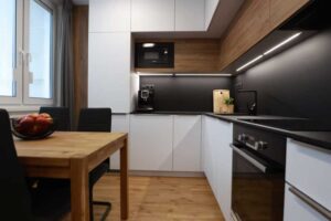 Moderní paneláková kuchyně v kombinaci bílé a dřeva s černou pracovní deskou a podsvícením, která působí čistě a nadčasově.