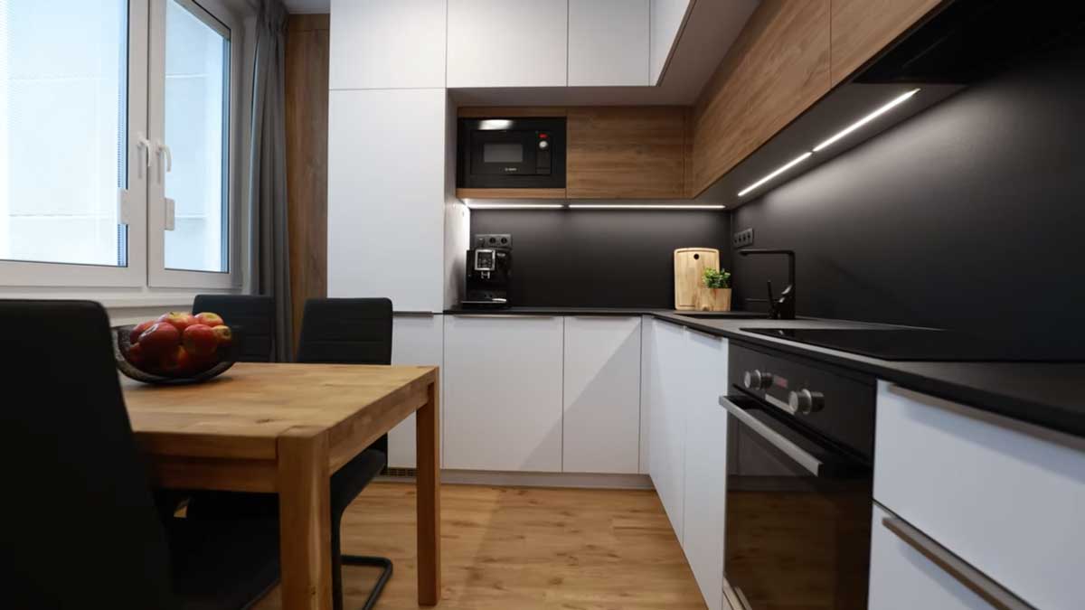 Moderní paneláková kuchyně v kombinaci bílé a dřeva s černou pracovní deskou a podsvícením, která působí čistě a nadčasově.