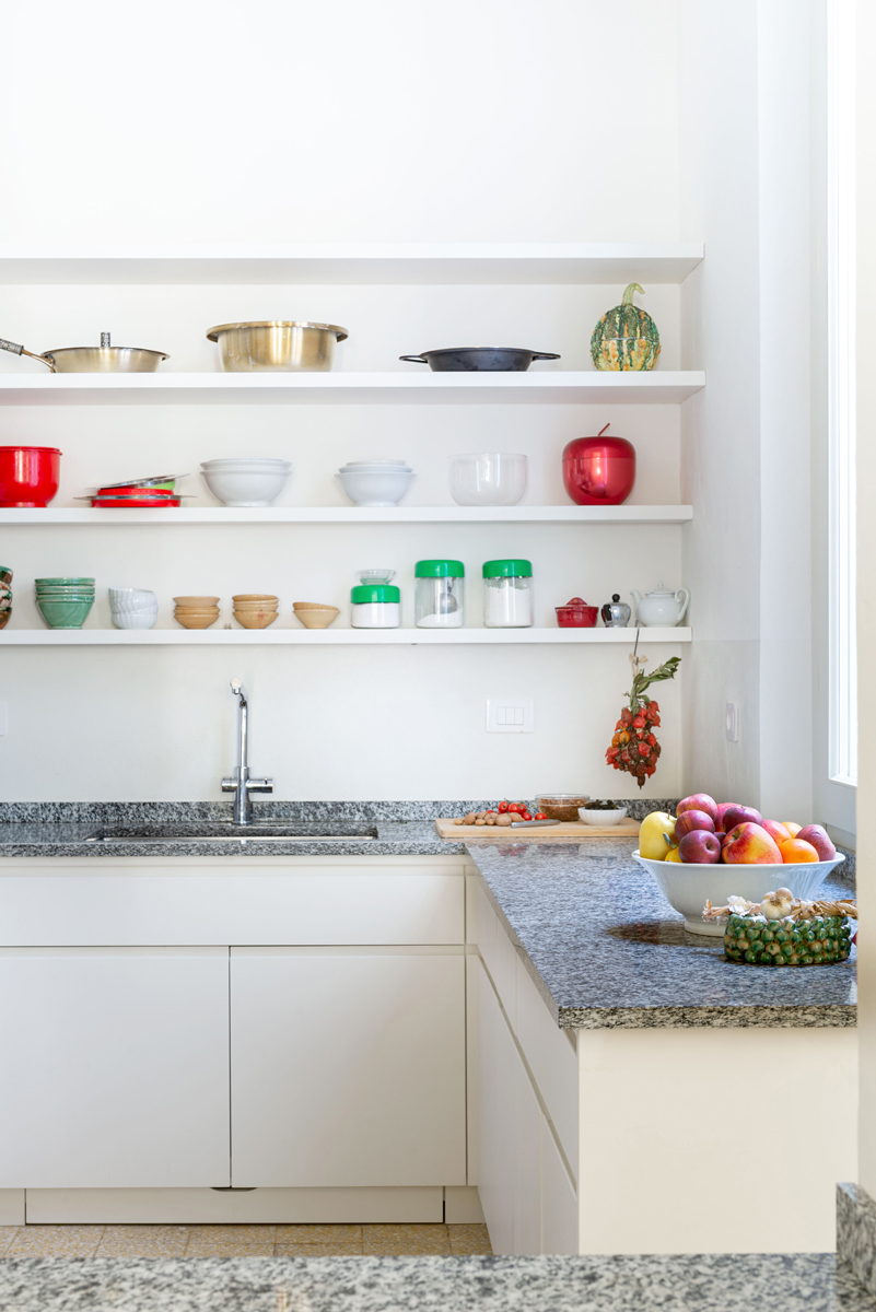 Kuchyňská linka s otevřenými policemi, žulovou deskou a sbírkou nádobí spojuje praktičnost s osobitou atmosférou domova.