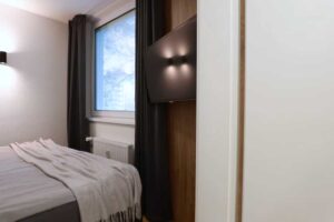 Jednoduchá ložnice s velkou postelí tmavými závěsy a tlumeným osvětlením vytváří klidnou atmosféru pro odpočinek.