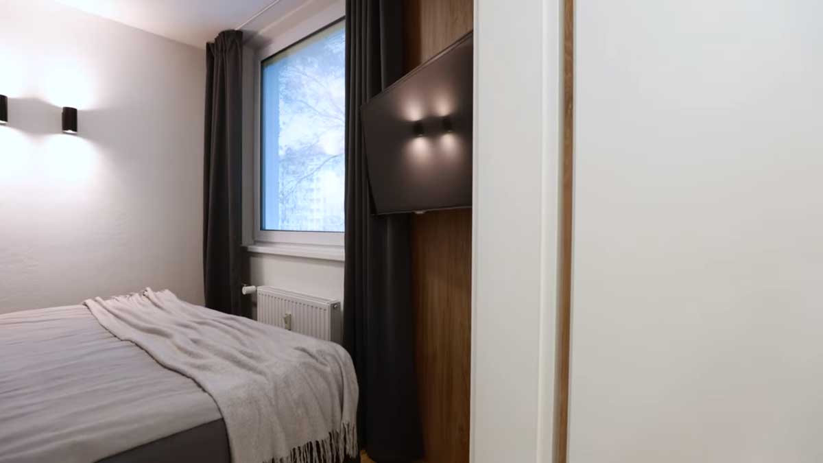 Jednoduchá ložnice s velkou postelí tmavými závěsy a tlumeným osvětlením vytváří klidnou atmosféru pro odpočinek.