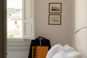 Ložnice s vysokým oknem, bílým ložním prádlem a jemnými dekoracemi působí klidně a elegantně.