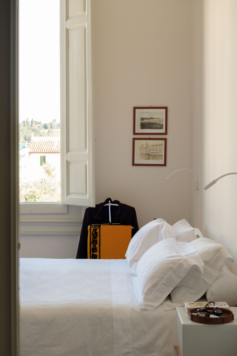 Ložnice s vysokým oknem, bílým ložním prádlem a jemnými dekoracemi působí klidně a elegantně.