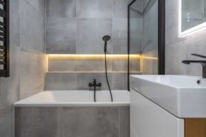 Moderní koupelna v imitaci betonu s černými doplňky a podsvícením působí elegantně a nadčasově.