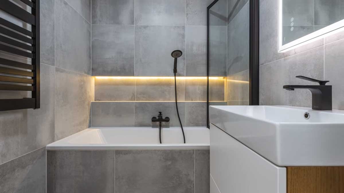 Moderní koupelna v imitaci betonu s černými doplňky a podsvícením působí elegantně a nadčasově.