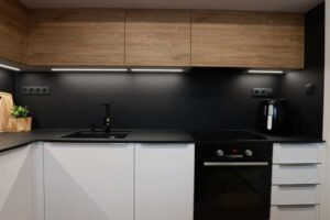 Nová kuchyňská linka v kombinaci bílé a dřeva s černou pracovní plochou vytváří čistý a funkční prostor.