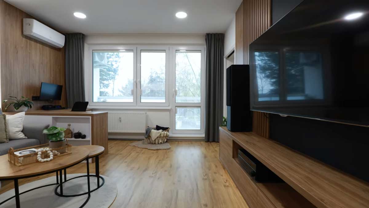 Světlý obývací pokoj s dřevěnou podlahou televizní stěnou a velkým oknem působí otevřeně a vzdušně.